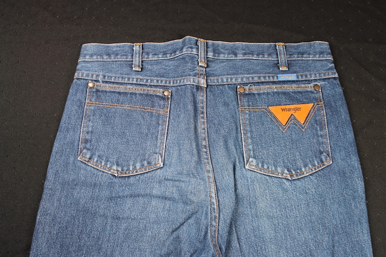 May include: A pair of blue denim jeans with a brown leather patch that says "Wrangler" on the back pocket.