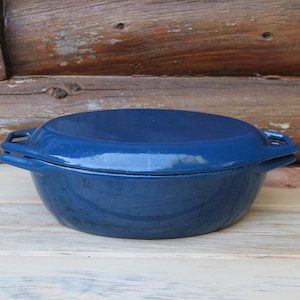 May include: A deep, oval-shaped blue enamelled Dutch oven with a matching lid. The pot features two integrated side handles and a smooth, glossy finish. The design is simple and functional, with a rounded base and a flat, fitted lid that sits securely on top of the vessel, providing a clean and uniform appearance for this kitchen cookware item.