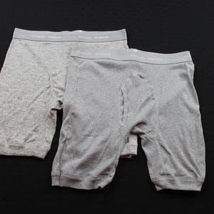 May include: Two pairs of heather grey boxer briefs featuring a wide elastic waistband with the text "GRAND ROMAR" printed in white. The underwear is constructed from a soft, knit fabric with a functional fly opening on the front panel.