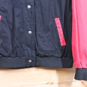 K&ouml;nnte beinhalten: Eine schwarze und rote Collegejacke mit Rei&szlig;verschluss und zwei Taschen. Die Jacke hat einen gerippten Strickkragen, B&uuml;ndchen und einen Bund.