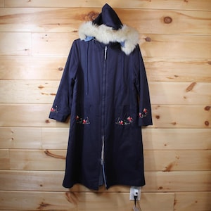 May include: A navy blue coat with a hood and faux fur trim. The coat features a zip closure and embroidered floral details on the sleeves and pockets. The coat is hanging on a wooden wall.