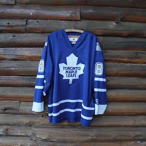 May include: A blue Toronto Maple Leafs hockey jersey with white stripes and accents. The jersey features the team's logo, a white maple leaf with the words "TORONTO MAPLE LEAFS" in white. The number "8" is on the sleeves.