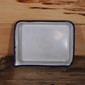 Puede incluir: Una bandeja para hornear de esmalte blanco con un borde azul. La bandeja es rectangular y tiene un borde ligeramente redondeado.