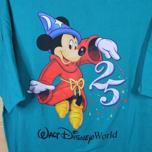 May include: A teal blue t-shirt featuring a graphic of Mickey Mouse dressed as a sorcerer. Mickey is holding a wand and pointing it at the number 25. The text "Walt Disney World" is printed below the graphic.