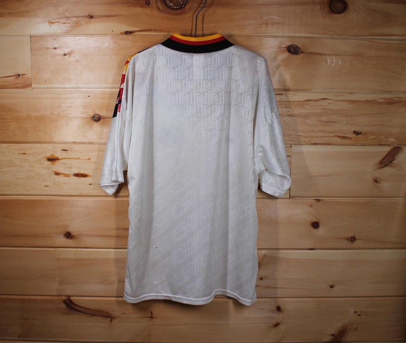 May include: White soccer jersey with yellow and black trim around the collar and sleeves. The jersey has a textured pattern and is made of a lightweight material.