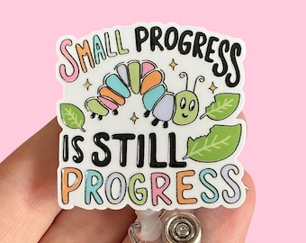 May include: White badge holder with a colorful cartoon caterpillar and the text "Small progress is still progress".
