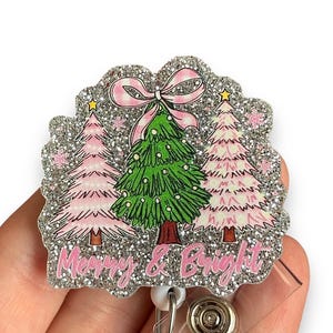 May include: Silver glitter Christmas tree badge reel with a pink bow and the text "Merry & Bright".