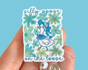 May include: A blue and green illustrated badge reel with a cartoon goose wearing a blue hat and the text "silly goose on the loose".