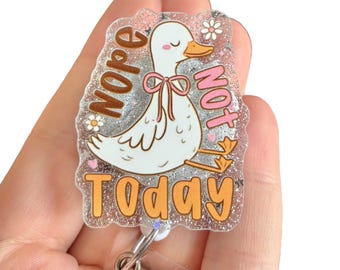 May include: A clear, glittery badge reel with a cartoon duck illustration. The duck has a pink bow and is surrounded by the words "Nope Not Today" in orange and pink lettering. The reel has a silver clip.