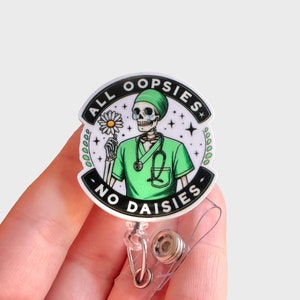 May include: A white round badge holder with a black and white graphic of a skeleton wearing a green surgical scrub and holding a daisy. The text on the badge holder reads "All oopsies no daisies".