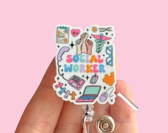 May include: A white badge holder with a colorful design featuring the words "SOCIAL WORKER" and various icons related to social work, such as a phone, a laptop, a heart, and a hand with raised fists. The badge holder is attached to a clear retractable badge reel.