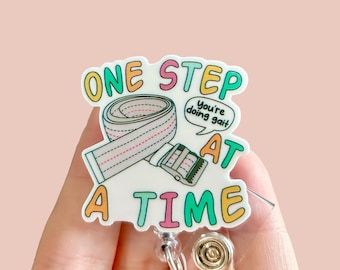 May include: A white badge holder with a colourful graphic that says "One Step At A Time" with a white belt and a speech bubble that says "You're doing gait".