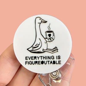 Puede incluir: Un carrete de insignia blanco con un dibujo lineal negro de un ganso sosteniendo una taza con un coraz&oacute;n. El texto "EVERYTHING IS FIGUREOUTABLE" est&aacute; debajo del ganso. El carrete de la insignia est&aacute; sostenido por una mano.