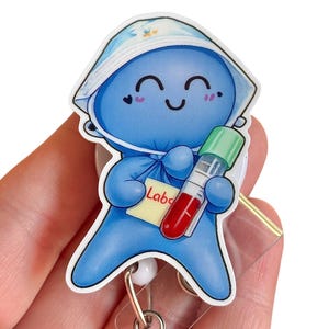 May include: A blue cartoon character badge reel with a smiling face, wearing a white hat with floral accents, holding a test tube with red liquid. The badge reel has a label that says "Lab".