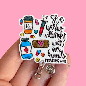 May include: A white badge reel with a medical theme. The design includes a prescription bottle, a syringe, pills, a bandage with a heart, and the text "She works willingly with her hands Proverbs 31:13."