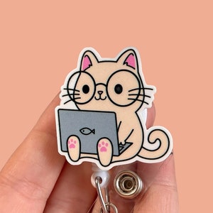 May include: A beige cat wearing glasses and sitting on a laptop with a fish icon. The cat is holding a laptop with its paws. The cat is attached to a white retractable badge holder.