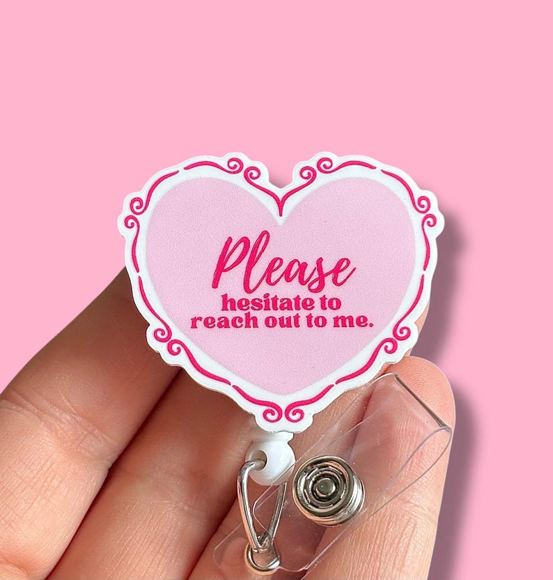 May include: Pink heart-shaped badge holder with a white border and the text "Please hesitate to reach out to me." in pink lettering.