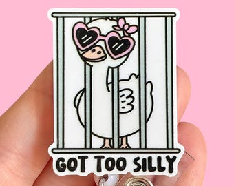 May include: A white cartoon goose wearing pink heart-shaped sunglasses is behind bars with the text "GOT TOO SILLY" on a white background. The goose is wearing a pink bow. The image is on a white retractable badge holder.
