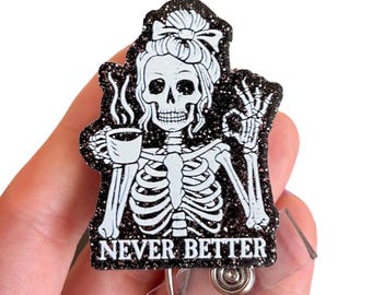 Könnte beinhalten: Ein schwarz-weißes Abzeichen mit einem Skelett mit einer Kaffeetasse und dem Text "NEVER BETTER". Das Skelett ist mit einer Schleife und Haaren versehen, und das Abzeichen hat einen glitzernden Rand. Ein durchsichtiger, einziehbarer Ausweishalter aus Kunststoff ist angebracht.