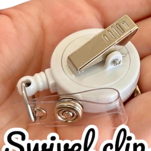 Puede incluir: Un carrete de insignia con clip giratorio blanco con un clip de metal plateado y una correa de pl&aacute;stico transparente. El texto "Swivel clip" est&aacute; escrito en fuente cursiva negra en la parte inferior de la imagen.