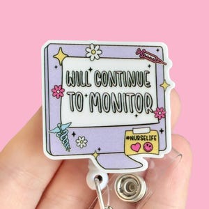 May include: A purple and white computer screen with the text "Will Continue To Monitor" and a pink sticky note with the text "#NURSELIFE" and a heart and smiley face. The computer screen is attached to a retractable badge reel.