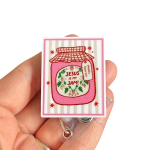 May include: A rectangular badge featuring a pink jar of jam with the text "JESUS IS MY JAM!" and a small tag that reads "SPREAD PSALM 34:8". The badge has a striped background and red star accents.