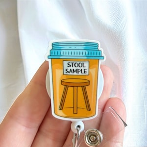 May include: A yellow and blue plastic badge holder with a cartoon image of a stool and the text "Stool Sample". The badge holder is attached to a retractable badge reel.