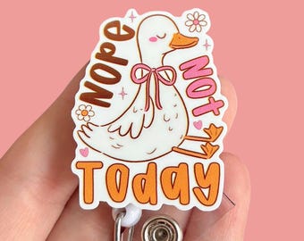 May include: A white duck badge reel with the words "Nope Not Today" in orange and pink. The duck has a pink bow and is surrounded by small flowers. The badge reel has a clear plastic retractable cord and a metal clip.