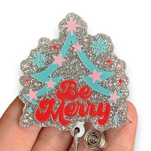 May include: Silver glitter Christmas tree with blue and pink accents and the text "Be Merry" on a retractable badge reel.
