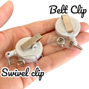 May include: Two white retractable badge holders with metal clips. One holder has a swivel clip and the other has a belt clip. The text "Belt Clip" and "Swivel Clip" are written in black on white backgrounds.