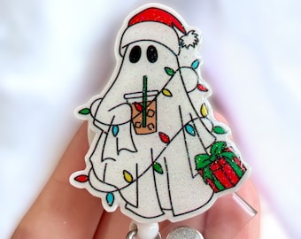 May include: A white glitter ghost wearing a red Santa hat and holding a cup of iced coffee. The ghost is decorated with colorful Christmas lights and a red and green gift box.