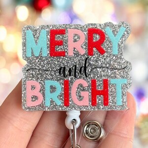 May include: Silver glitter badge holder with a clear plastic badge holder and a retractable badge reel. The badge holder features the text "Merry and Bright" in red, pink, and blue glitter letters.