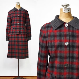 May include: Vintage plaid skirt suit in red, black, and gray. The jacket has a gray knit collar and matching cuffs, with three buttons down the front. The skirt is knee-length. The suit is displayed on a mannequin.