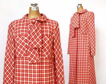 Könnte beinhalten: Ein Vintage-Mantelkleid mit rot-weißem Karomuster und passendem Schleifenkragen. Das Kleid hat lange Ärmel und einen knielangen Saum. Der Stoff hat ein strukturiertes Aussehen, und das Kleid wird auf einer Schaufensterpuppe präsentiert.