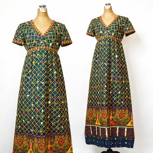 May include: A long, blue maxi dress with a geometric pattern of yellow and green squares and small red and white flowers. The dress has a V-neckline, short sleeves, and a fitted bodice. The hemline is decorated with a band of orange, yellow, and red geometric shapes.
