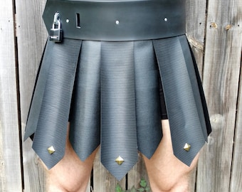 May include: A black leather skirt with a pleated design and a black leather belt with a silver padlock. The skirt has gold-colored studs on the bottom edge.