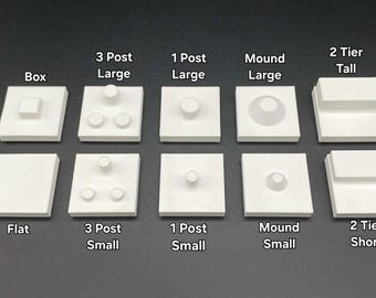 May include: Ten white square display bases arranged in two rows. Top row: Box, 3 Post Large, 1 Post Large, Mound Large, 2 Tier Tall. Bottom row: Flat, 3 Post Small, 1 Post Small, Mound Small, 2 Tier Short. Each base features distinct geometric shapes.