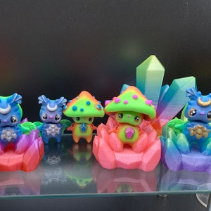 May include: Five colorful figurines with mushroom-shaped heads and crystal-like bases. The figurines are made of plastic and have a whimsical, fantasy-inspired design.