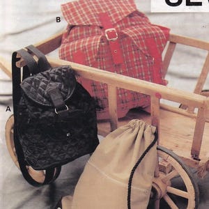 May include: A sewing pattern for back packs, featuring three different styles. One is a black quilted backpack, another is a red plaid backpack, and the third is a tan drawstring bag. The pattern is labeled "Pattern 2379" and "KWIK SEW."