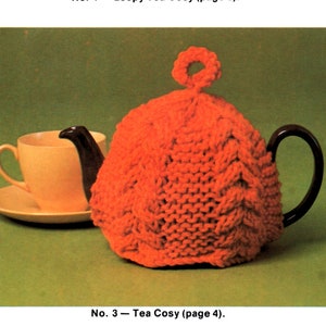 Puede incluir: Tres patrones de calienta-teteras de punto. El primero es un calienta-tetera azul de bucles con un pompón en la parte superior. El segundo es un calienta-tetera rojo de punto. El tercero es un calienta-tetera a rayas con rayas marrones, rojas y crema.