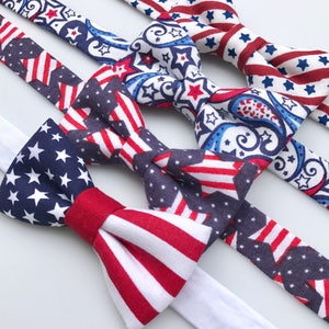 May include: Three bow ties with red, white, and blue patriotic patterns. One bow tie has a paisley pattern with stars, another has red and white stripes, and the third has a blue and white stars pattern with red stripes.