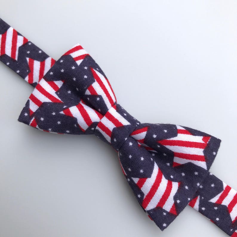 May include: A navy blue bow tie with a repeating pattern of red, white, and blue American flags.