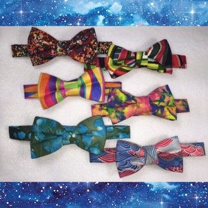 May include: Six colorful bow ties with different patterns. The bow ties are made of fabric and have a variety of colors, including red, blue, green, yellow, and orange.