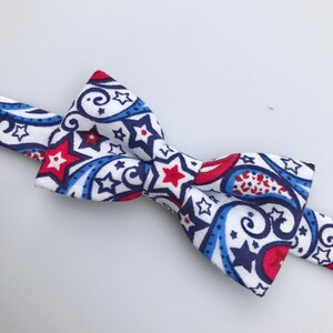 May include: A white bow tie with a red, blue, and white paisley pattern featuring stars.