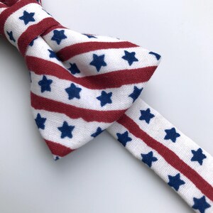 May include: A red, white, and blue bow tie with a striped pattern and white stars. The bow tie is made of fabric and is suitable for a special occasion.