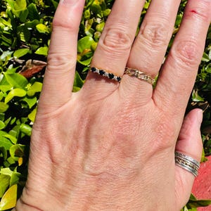 May include: A gold ring featuring a row of five small black stones alternating with tiny clear stones, worn alongside a gold chain-link band on the middle finger and a stack of thin silver and gold bands on the thumb.