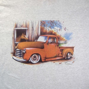 May include: A vintage orange pickup truck with a wooden barn in the background. The truck has a horse peeking out of the barn window.