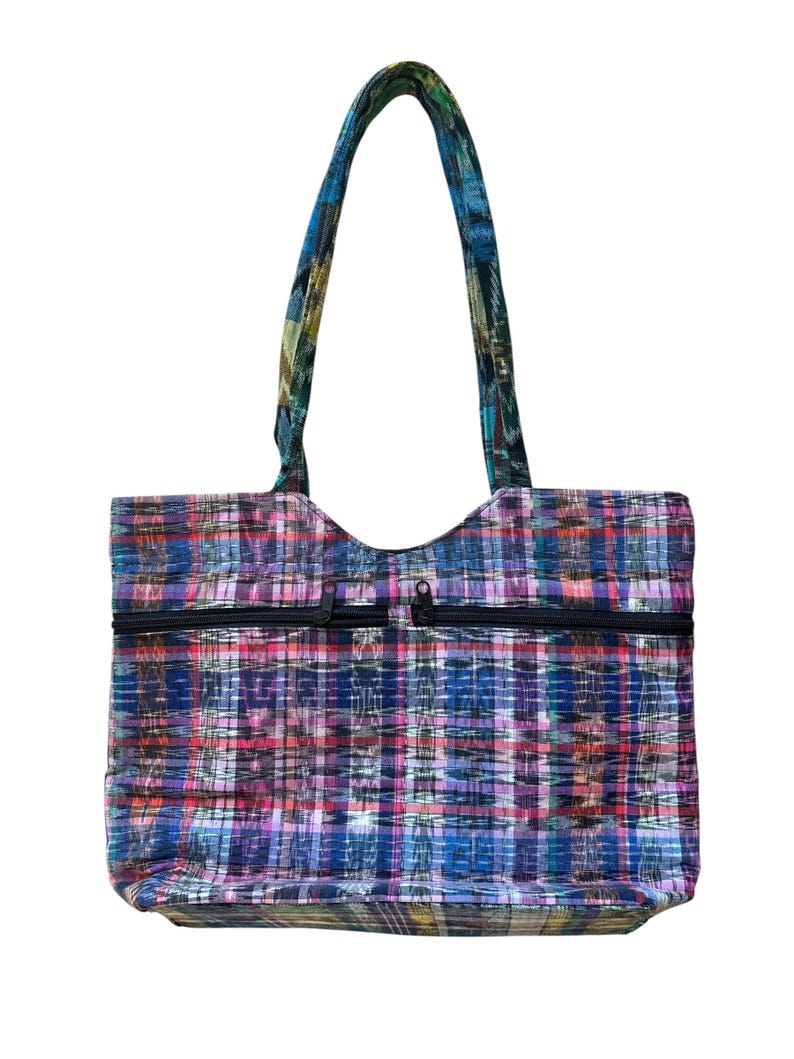 May include: A multi-coloured tote bag with a plaid design in blue, purple, pink, and green. The bag features two black zipped pockets and a matching patterned handle. The bag is designed for carrying items.