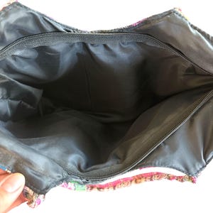 May include: An open tote bag with a colourful, patterned exterior. The bag's interior is black, and it has a black zip closure. The exterior is made of woven fabric in pink, green, and tan.