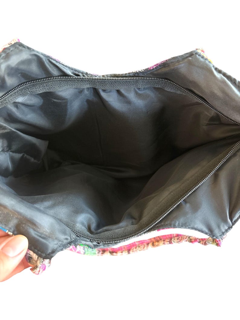 May include: An open tote bag with a colourful, patterned exterior. The bag's interior is black, and it has a black zip closure. The exterior is made of woven fabric in pink, green, and tan.